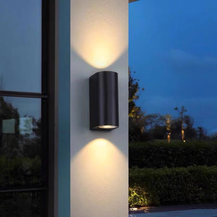 Black cylindrical outdoor LED wall light mounted on building exterior night view